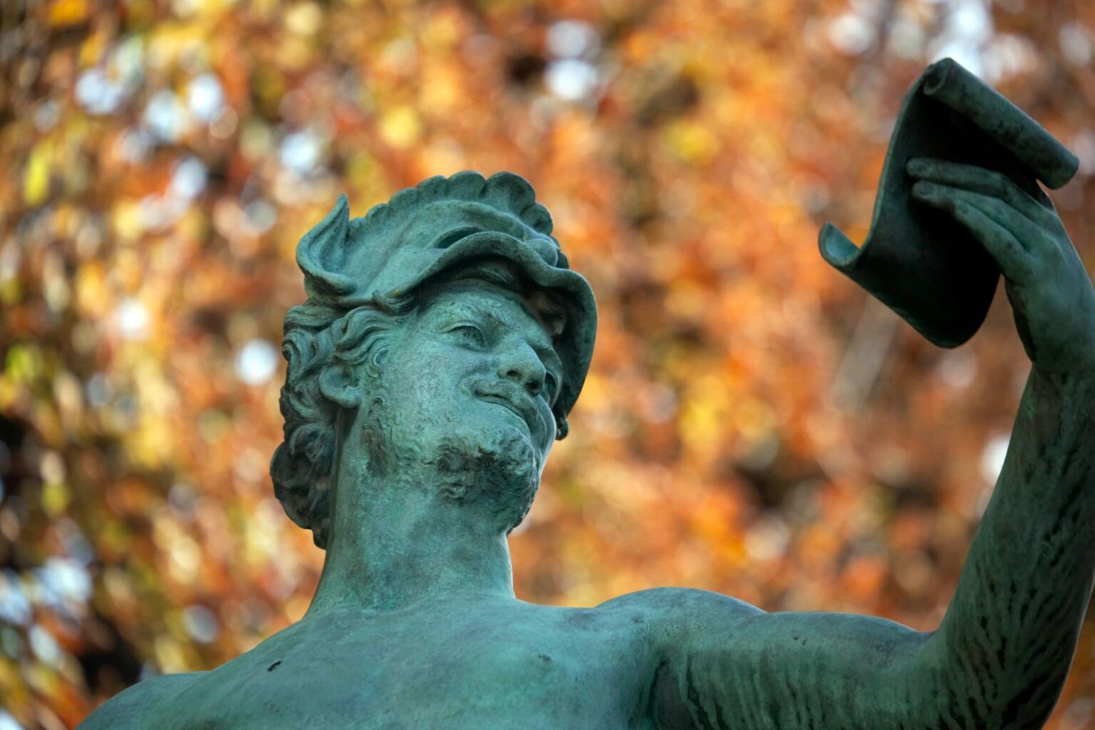 Cumprimentos (salutoj) em esperanto Estátua de bronze esverdeado de um homem de barba erguendo o chapéu, com folhas de outono ao fundo