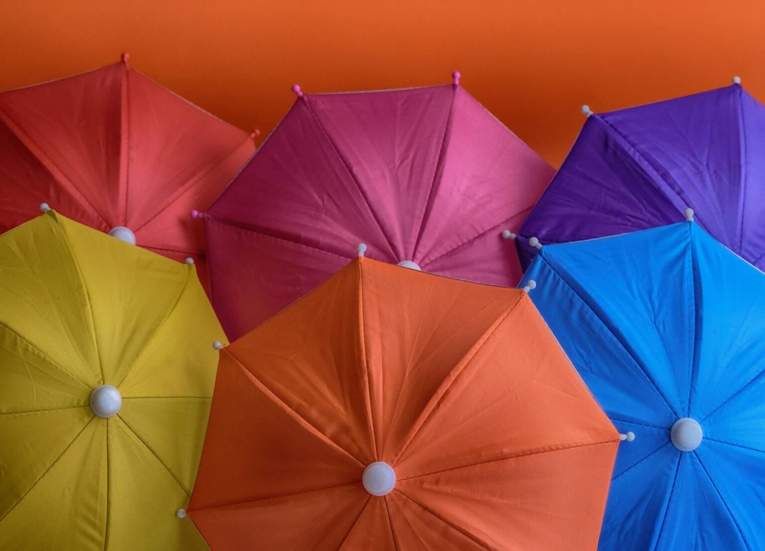 Guarda-chuvas abertos vermelho, rosa, roxo, amarelo, laranja e azul vistos de cima sobre um fundo laranja