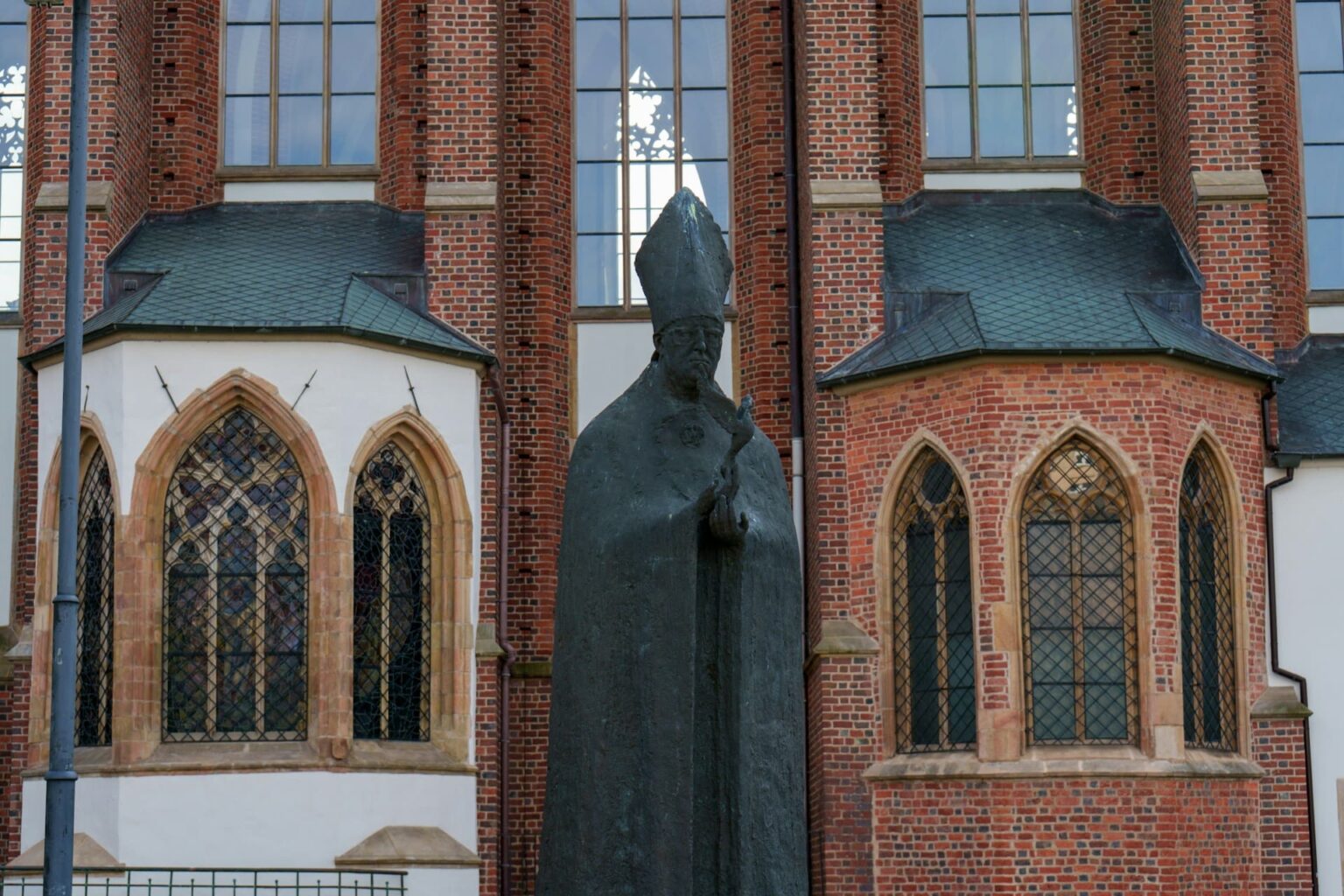 Dias da semana e meses (semajntagoj kaj monatoj) em esperanto Estátua escura de um bispo de mitra diante de uma igreja de tijolos vermelhos com janelas góticas