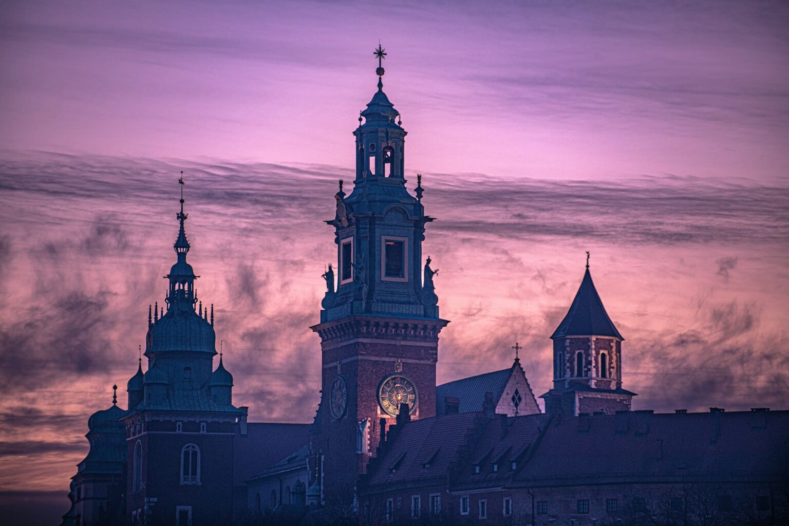 Verbos transitivos e intransitivos em esperanto Torres de uma catedral com relógio e cúpulas em silhueta contra um céu violeta ao entardecer