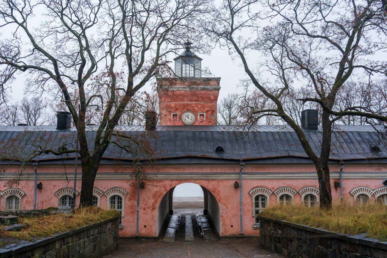 Edifício rosa com torre de relógio e passagem em arco, entre árvores sem folhas