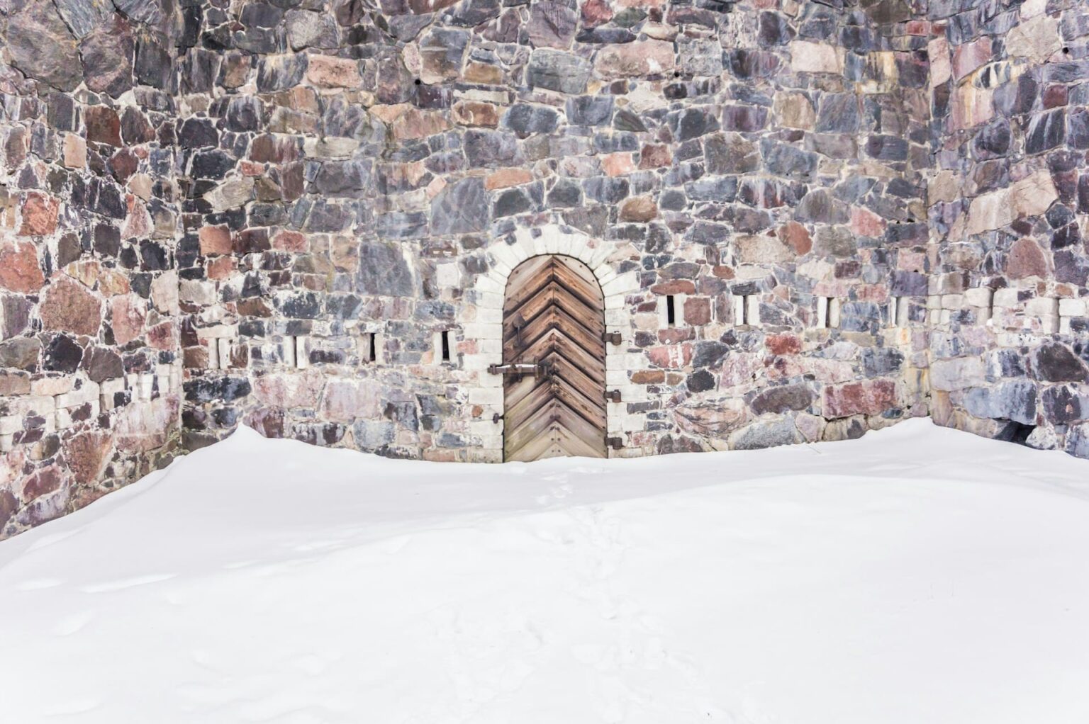 Muro de pedra com porta de madeira, cercado de neve