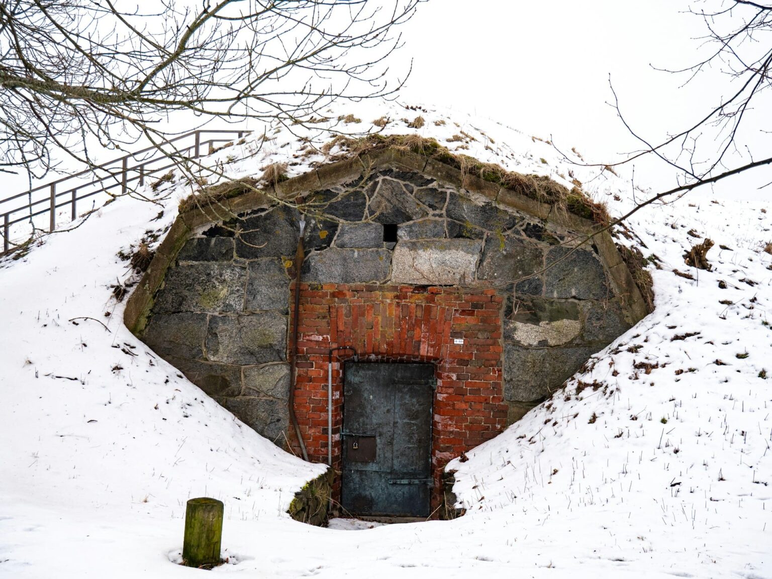 Entrada de pedra e tijolo com porta de metal, num barranco coberto de neve