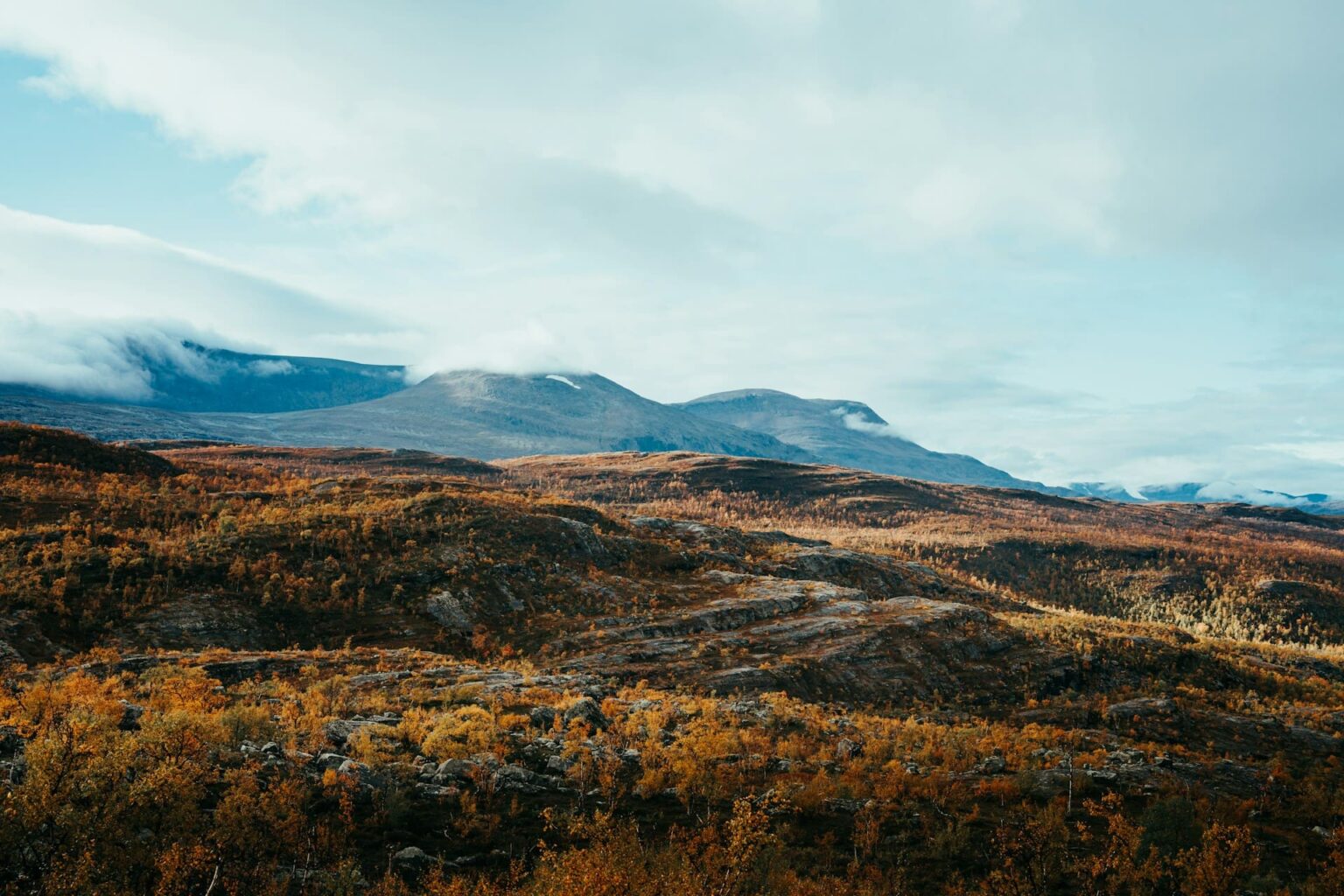 Montanhas e vegetação com cores de outono sob nuvens