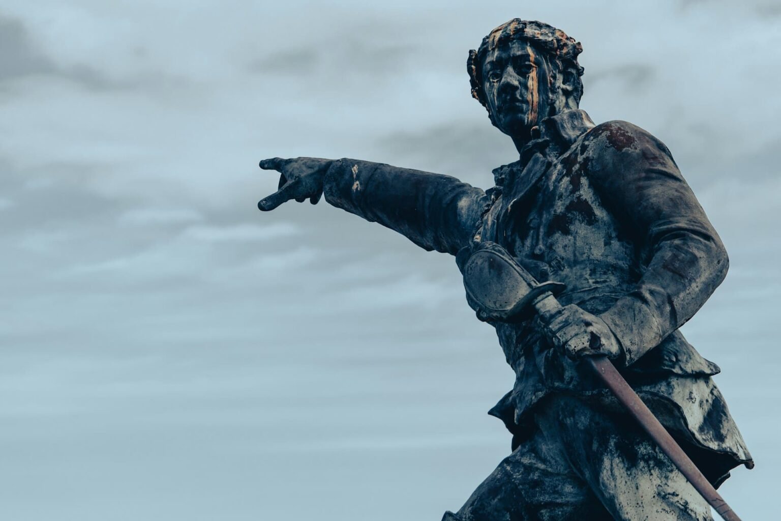 Demonstrativos (démonstratifs) em francês Estátua de bronze de um homem apontando com o braço estendido e segurando uma espada
