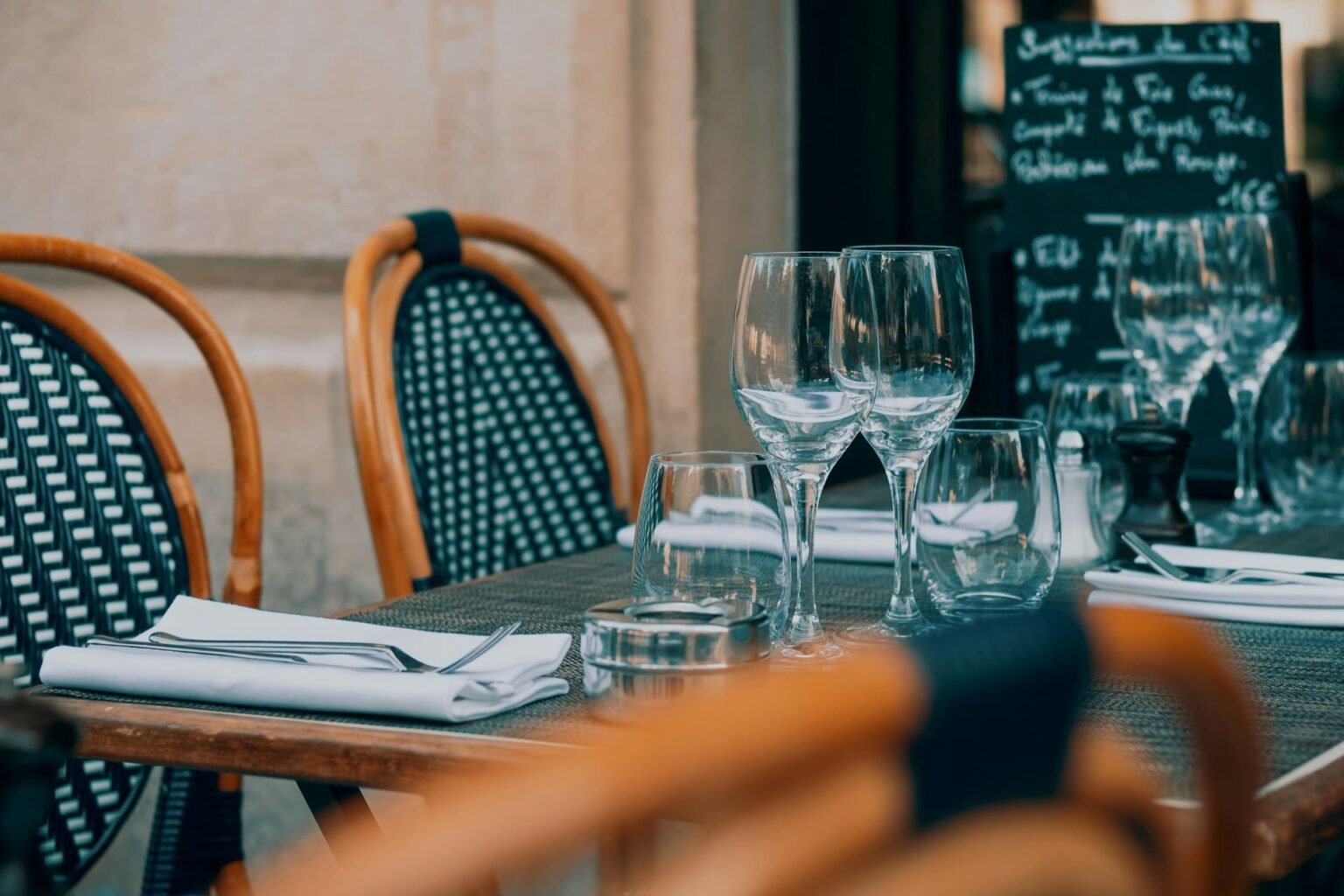 Vocabulário de restaurante em francês Mesa de terraço de restaurante com taças, copos e guardanapos, e um quadro com as sugestões do chef ao fundo