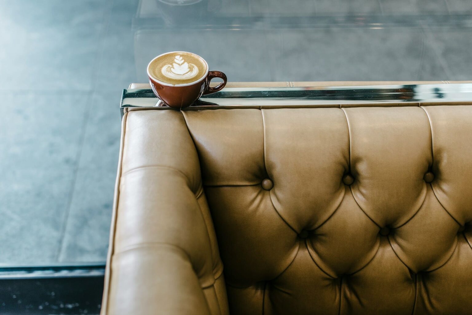 Xícara de cappuccino sobre o braço de um sofá de couro capitonê