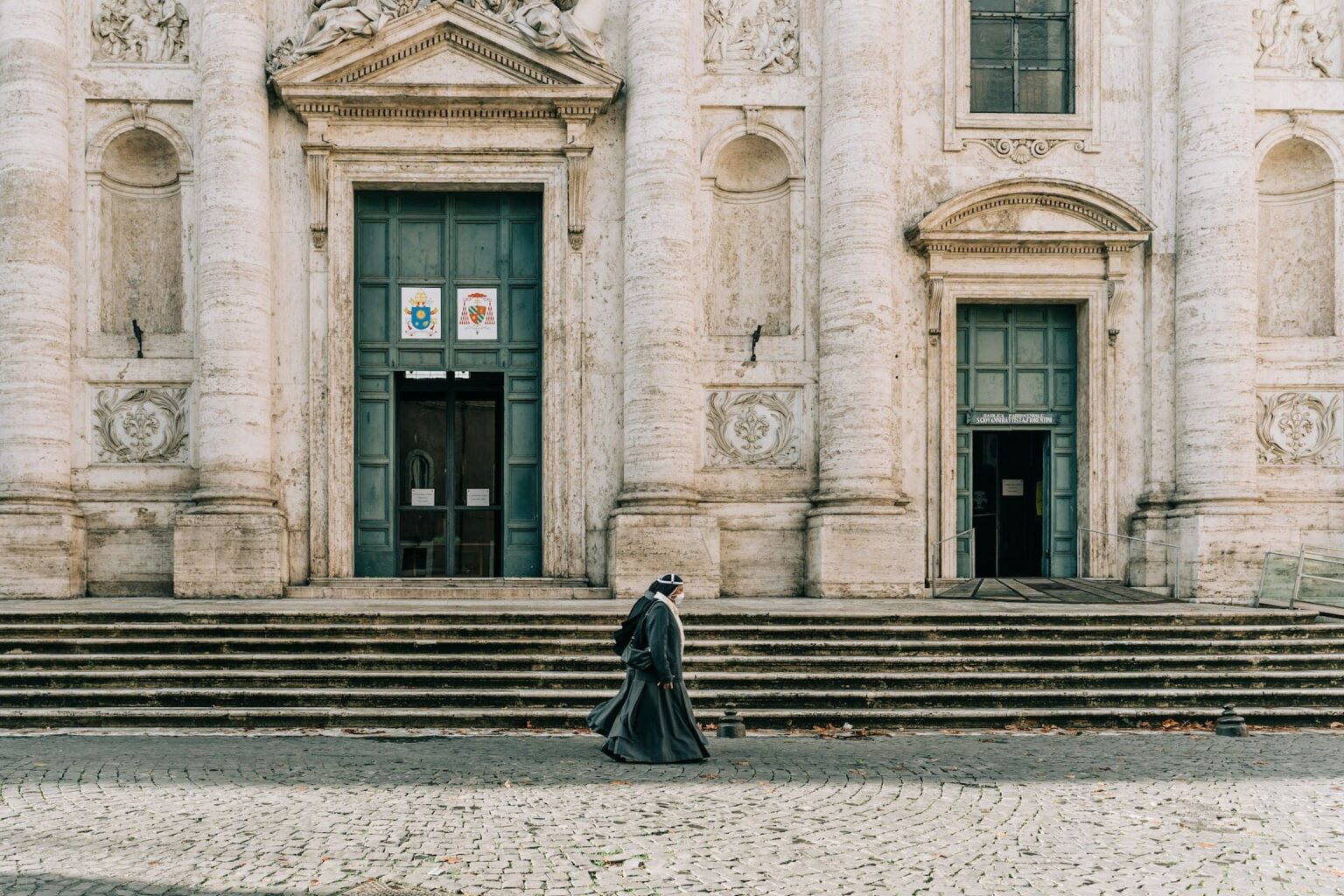 Freira caminhando diante da escadaria e da fachada de uma igreja