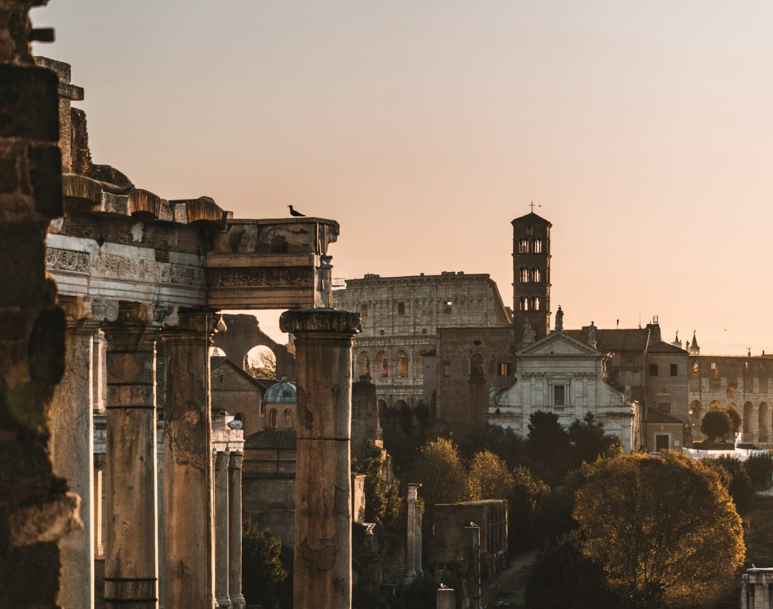 Colunas do Fórum Romano com o Coliseu ao fundo, ao pôr do sol