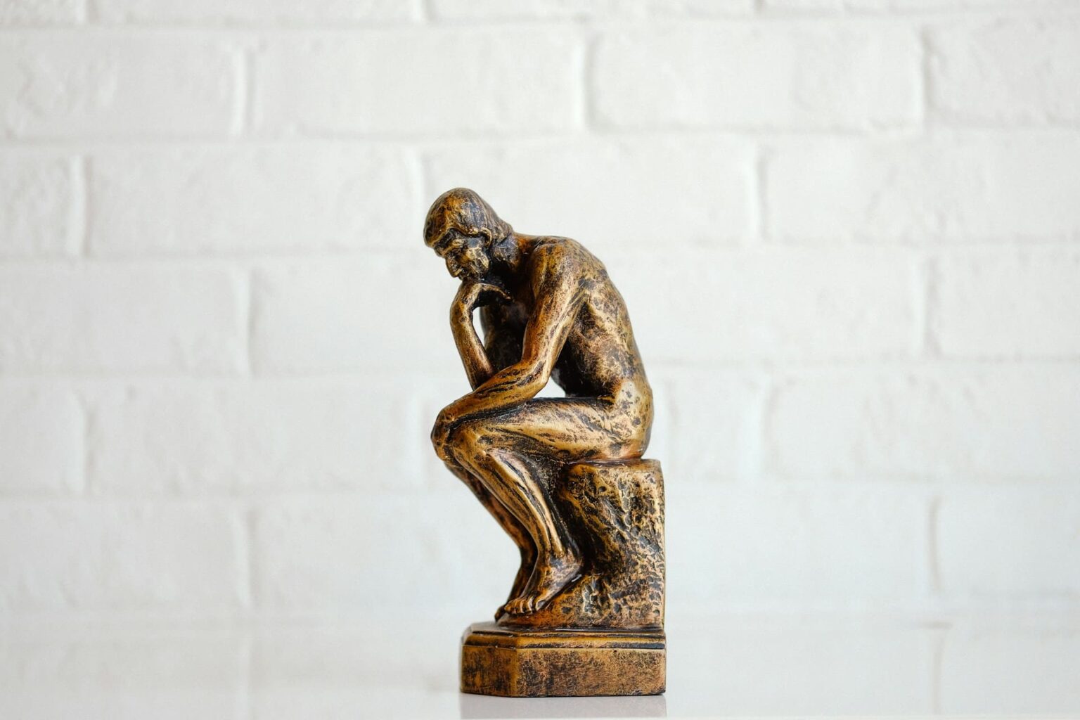 Como fazer perguntas em italiano Pequena réplica em bronze de O Pensador, de Rodin, diante de uma parede branca