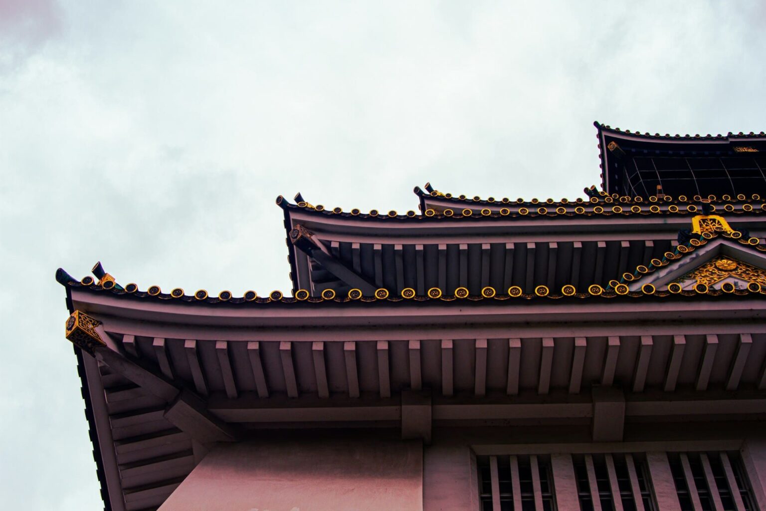 Beirais em camadas de um castelo japonês, com telhas de pontas douradas, contra o céu nublado