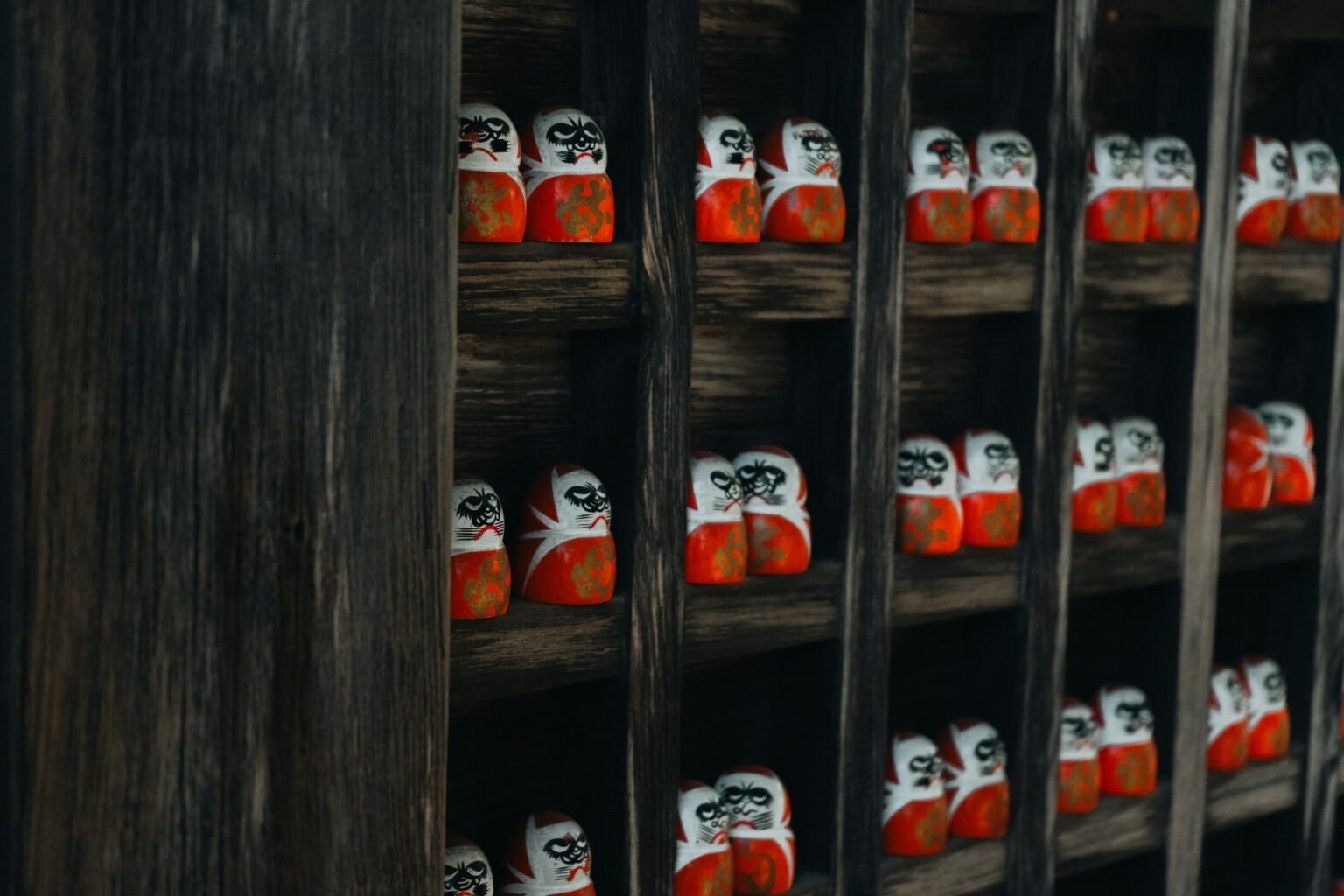Pequenos bonecos daruma vermelhos e brancos enfileirados em prateleiras de madeira escura
