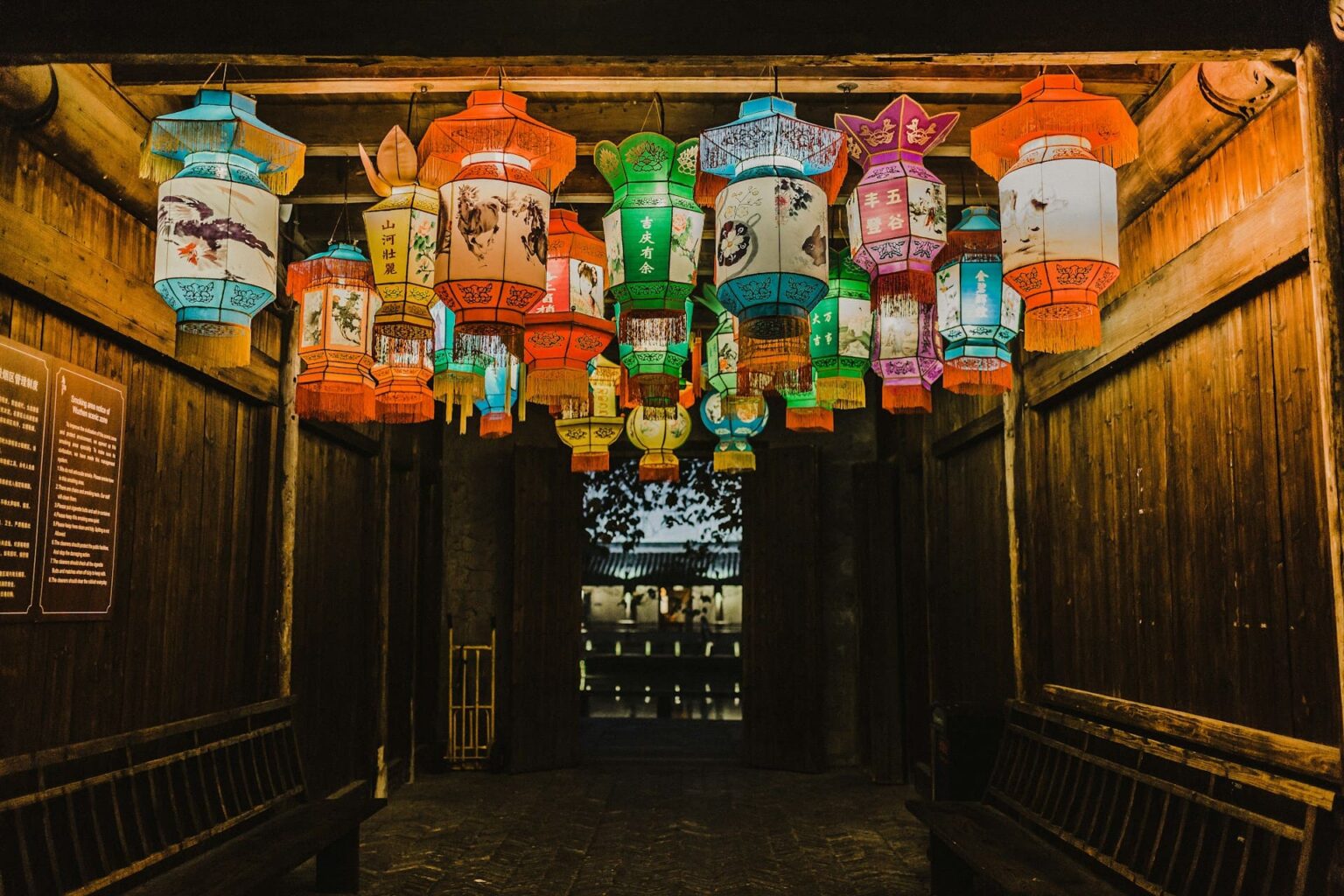 Lanternas coloridas pintadas com flores, cavalos e caracteres chineses, penduradas no teto de um corredor de madeira