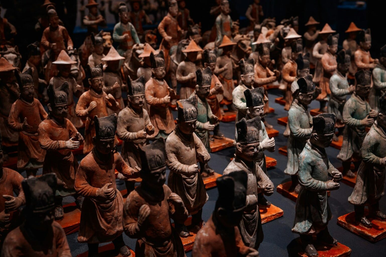 Fileiras de estatuetas antigas de cerâmica pintada, de figuras com chapéus altos e cônicos, sobre bases vermelhas