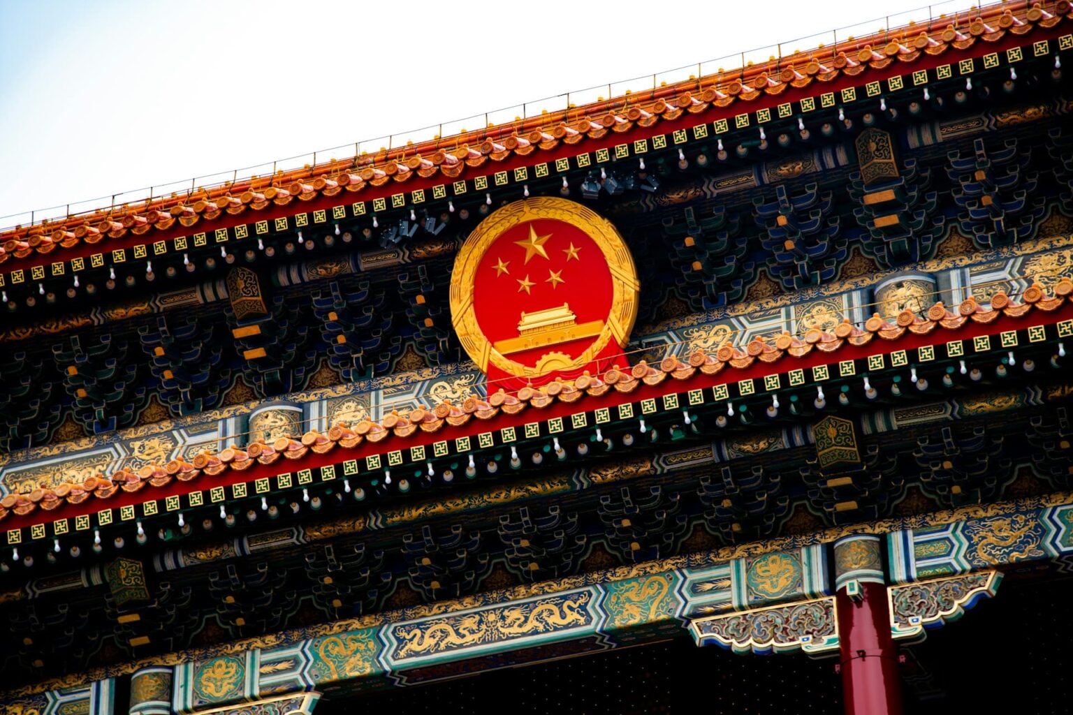 Emblema nacional da China na fachada de um portão, entre beirais pintados com dragões dourados