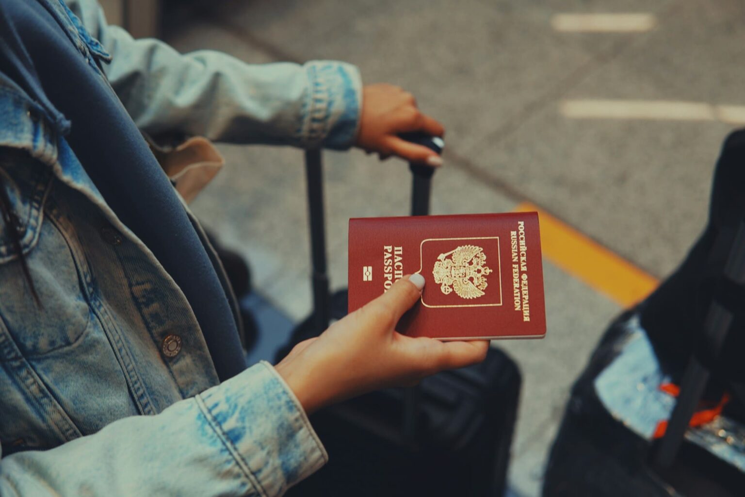 Mão segurando um passaporte russo, ao lado de uma mala de viagem