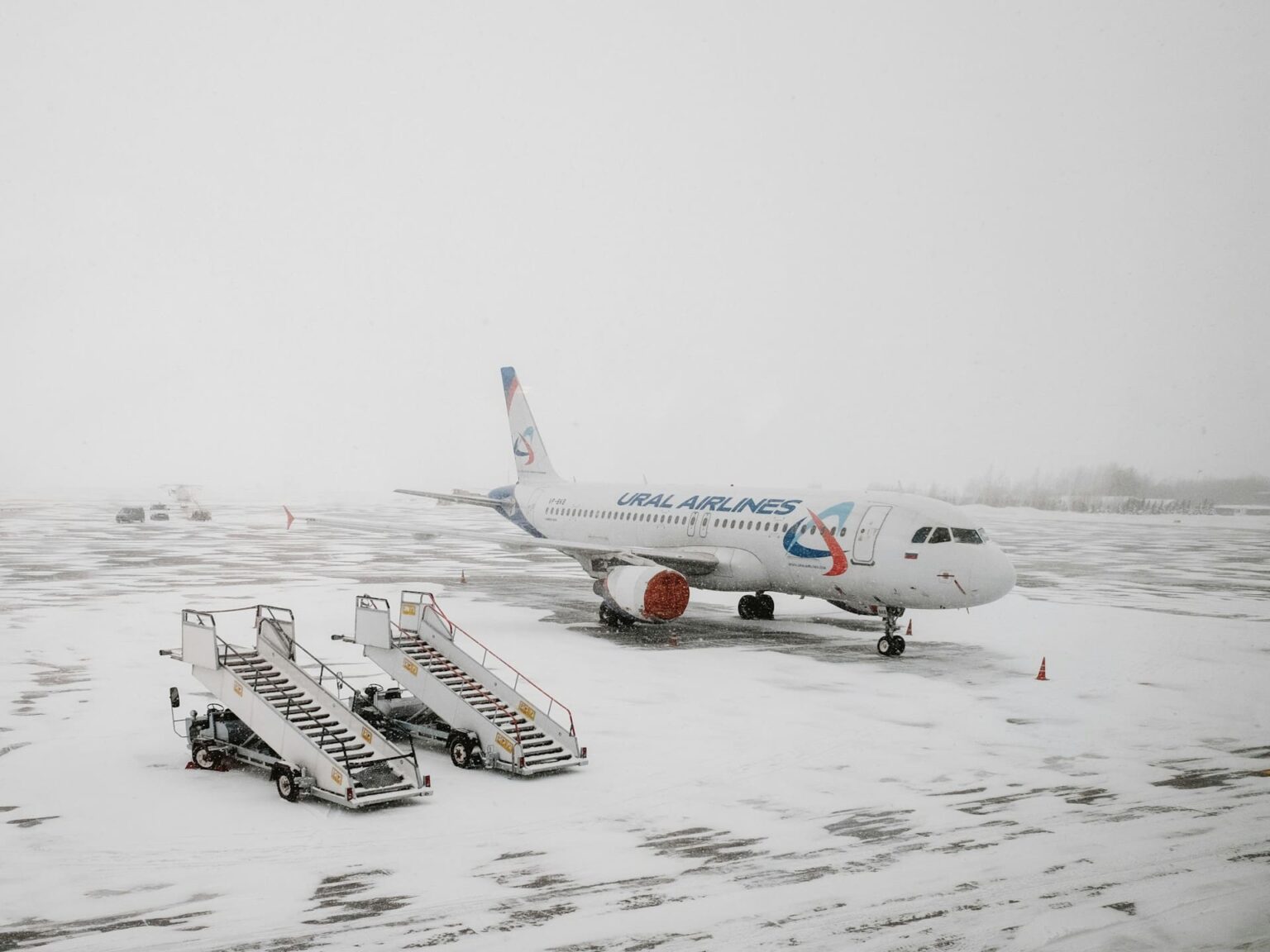 Avião de passageiros parado num aeroporto coberto de neve, ao lado de duas escadas de embarque