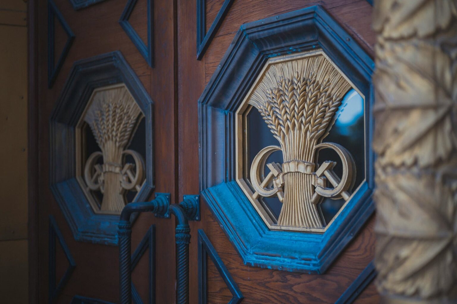 Porta de madeira com ornamentos dourados de feixes de trigo em molduras octogonais azuis