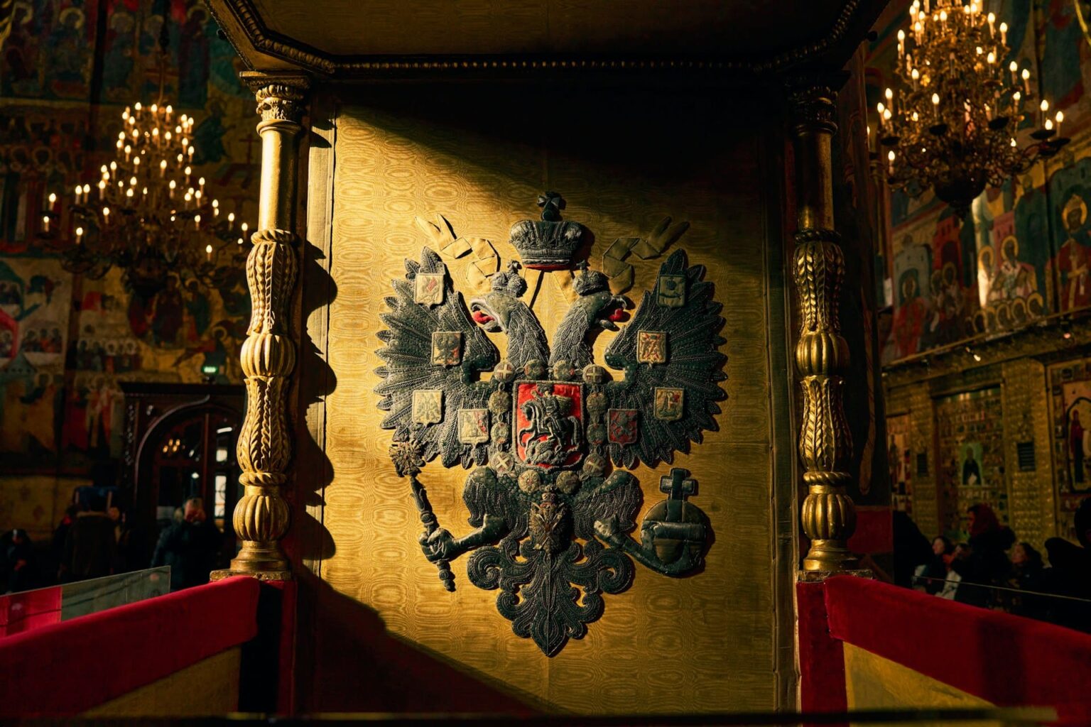 Brasão com a águia bicéfala russa, bordado num painel dourado no interior de uma igreja com ícones e lustres