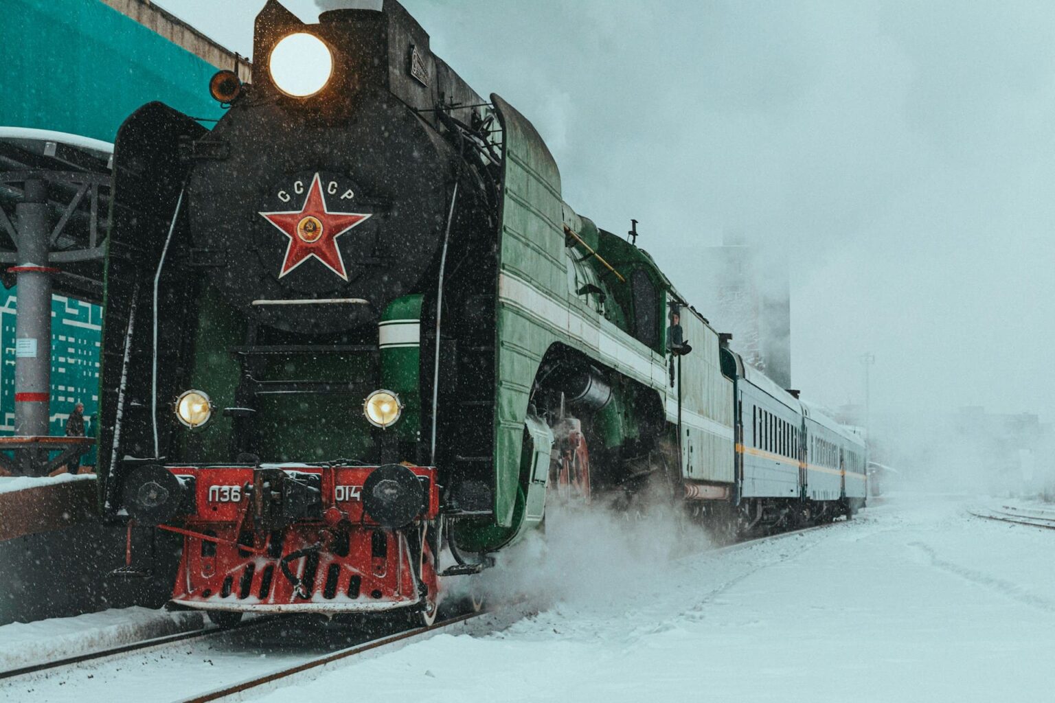 Locomotiva a vapor soviética, verde, com a estrela vermelha e a inscrição СССР, numa estação coberta de neve