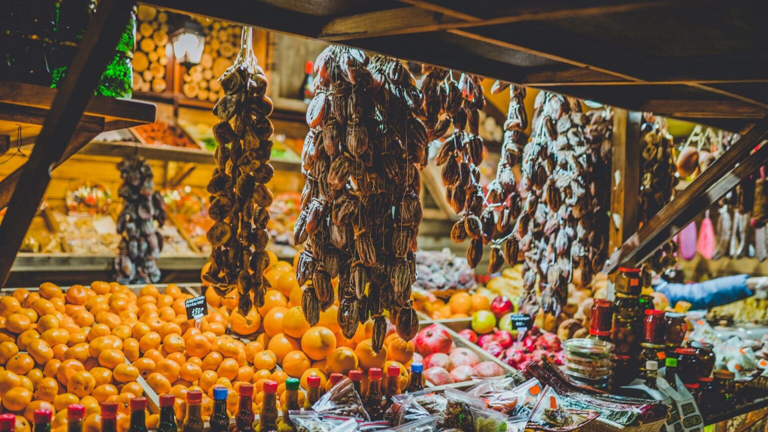 Barraca de feira com tangerinas, romãs, frutas secas penduradas e potes de conserva