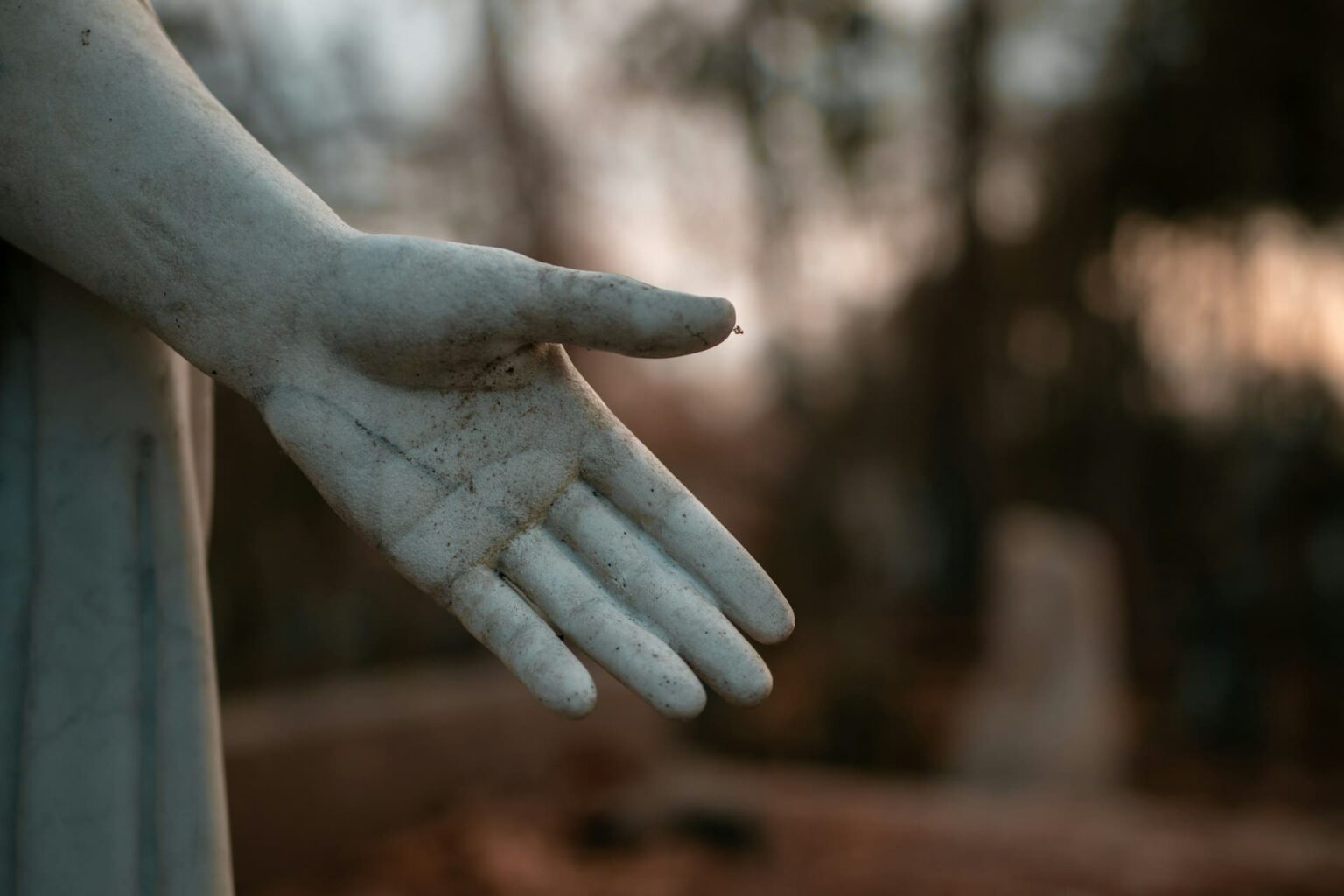 Como falar “por favor” em ucraniano Mão de uma estátua de pedra estendida com a palma para cima, com árvores desfocadas ao fundo