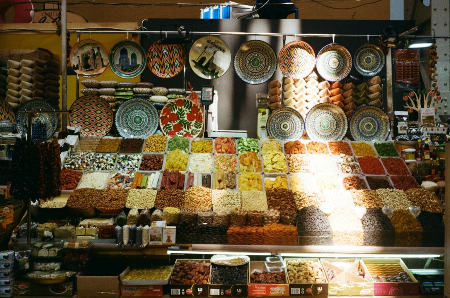 Banca de mercado com frutas secas, castanhas e temperos, e pratos de cerâmica pintados ao fundo