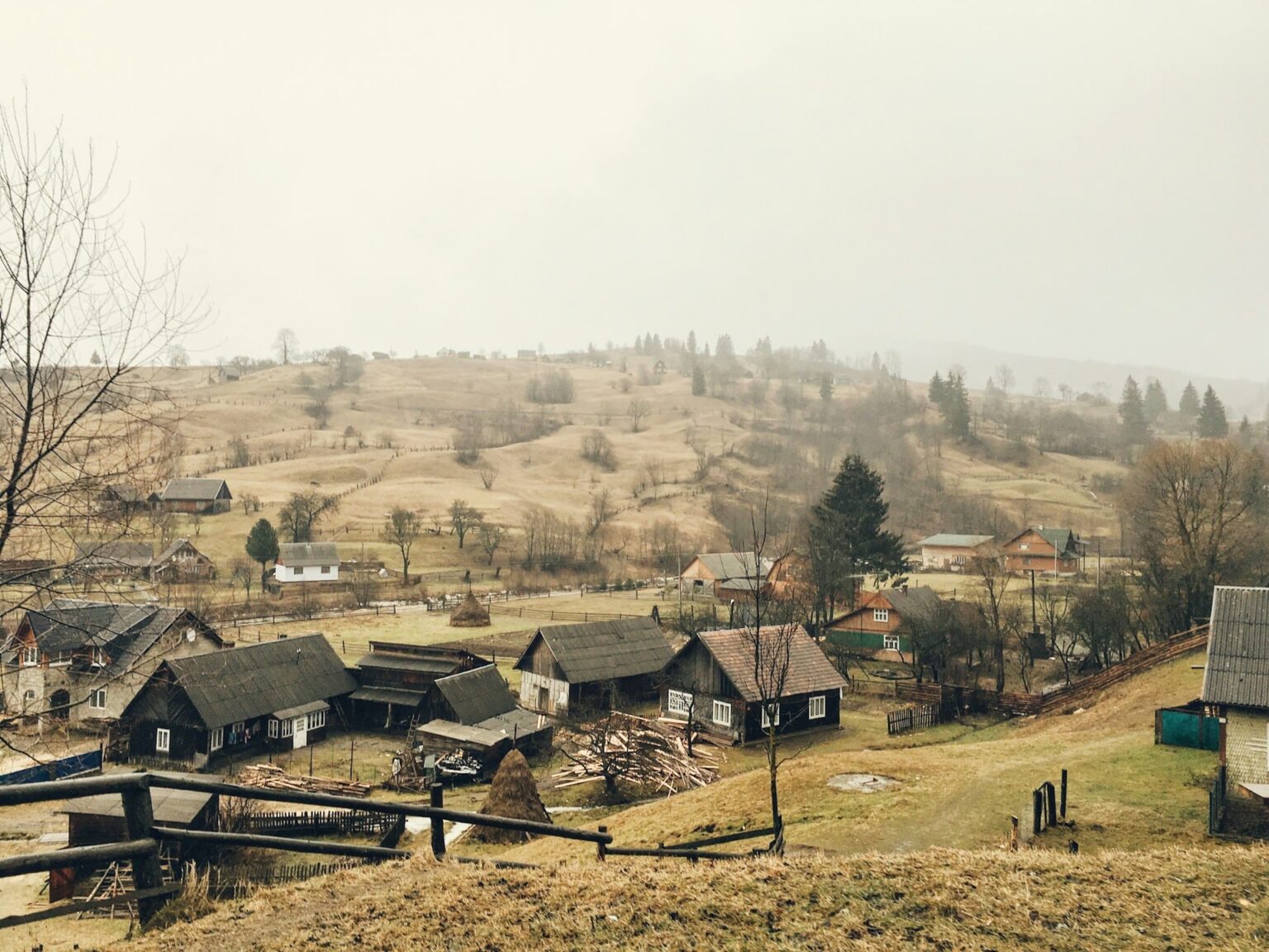 Aldeia com casas de madeira entre colinas, num dia de neblina